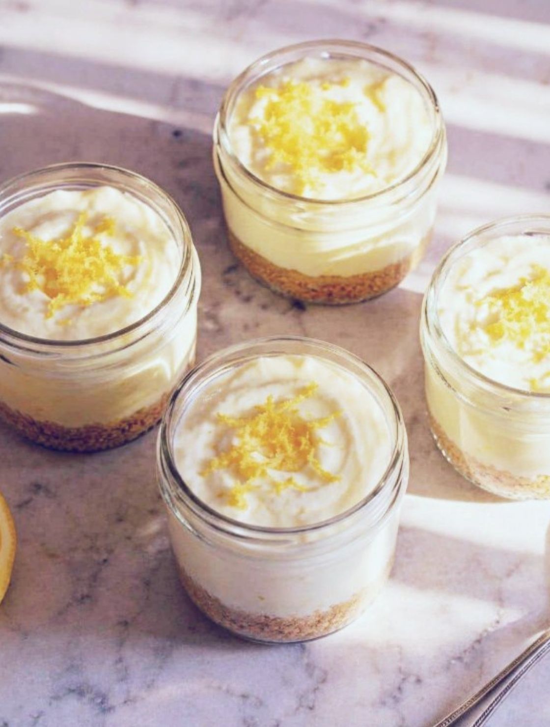 Four No-Bake Keto Lemon Cheesecake Cups topped with fresh lemon zest, served in small mason jars as a creamy low-carb dessert.